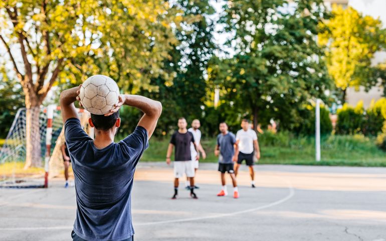 Man taking a throw in soccer game played on urban soccer field.