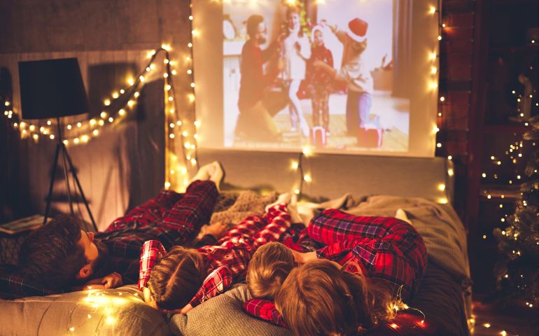 happy family in checkered pajamas: mother father and children watching projector, TV, movies with popcorn in christmas holiday evening at home