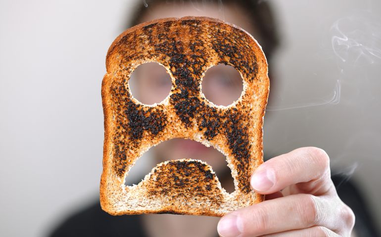 Man holding up a burnt slice of toast with an unhappy smiley conept for bad start to the day