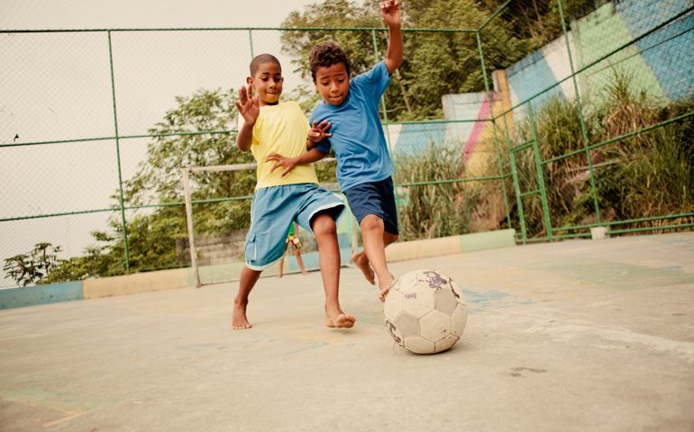 Two boys from the favelas in Rio de Janeiro challenge each other for the soccer ball on a concrete pitch.