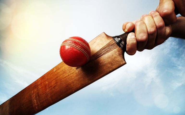 Cricket batsman hitting a ball shot from below against a blue sky