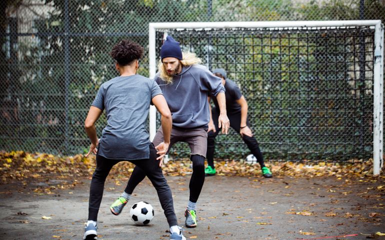 Confident young man dribbling ball from opponent. Player is standing at goal post. They are in sportswear.