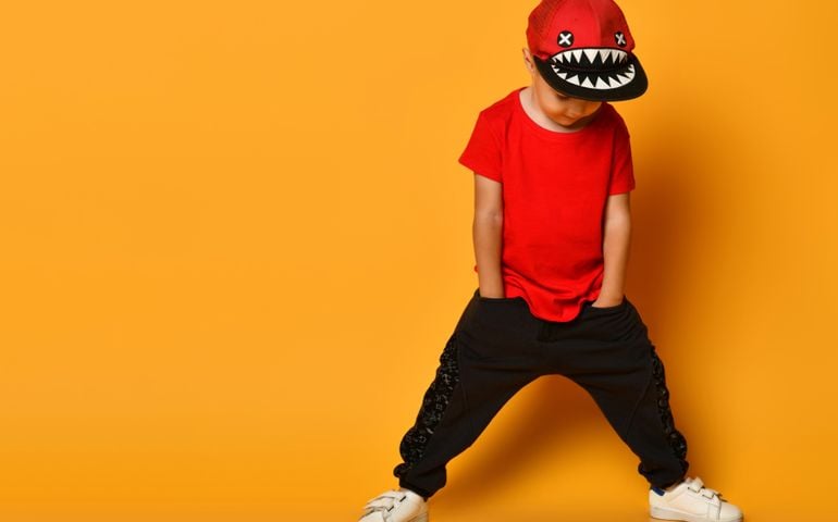 Little cute 4 year old boy in wide dark pants with pockets and a red T-shirt. A merry cap with shark teeth.