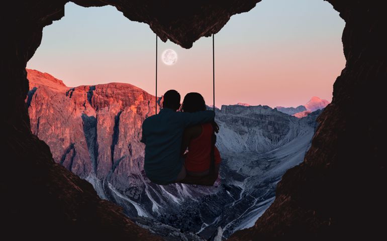 Composition of the Alps mountains during sunset with full moon and couple on swing from a heart shape cave.