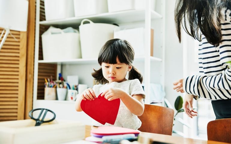 Young girl looking at paper hearts while making Valentines Day cards in home