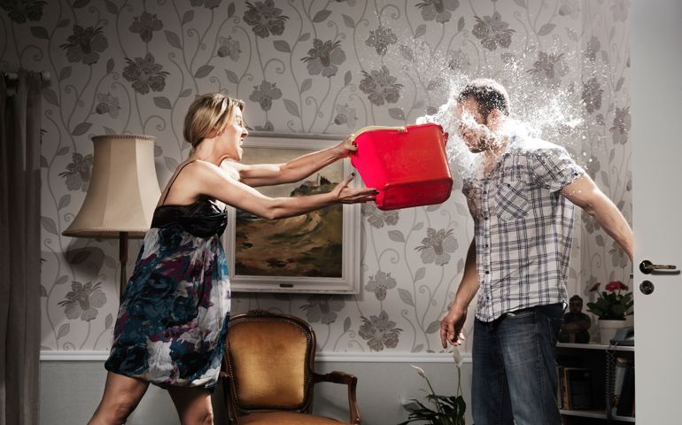 young woman thowing a bucket of water at her partner, in the living room