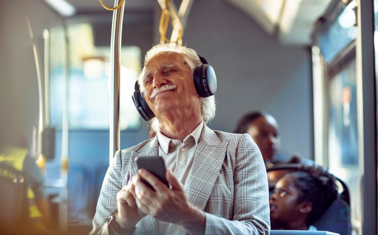 Close up of a senior man listening to music on his phone while commuting in a bus