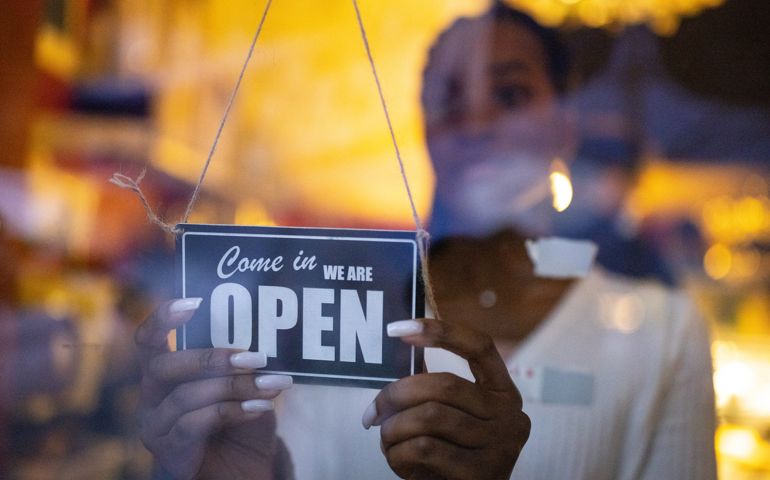 Woman turning an open sign on glass front door of coffee shop. Business owner hanging an open sign at a cafe.