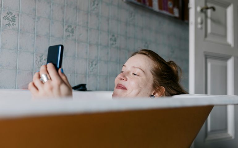 A woman taking a bath and smiling while messaging someone she met on a dating app using her smartphone.