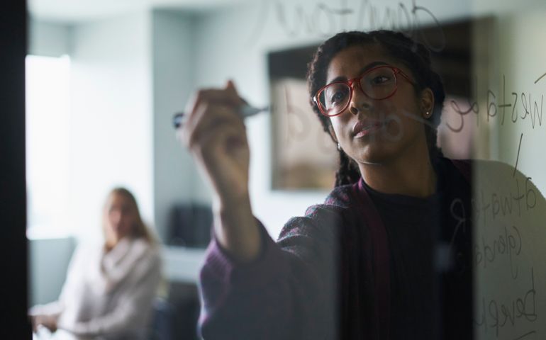 Businesswoman writing on glass wall during meeting