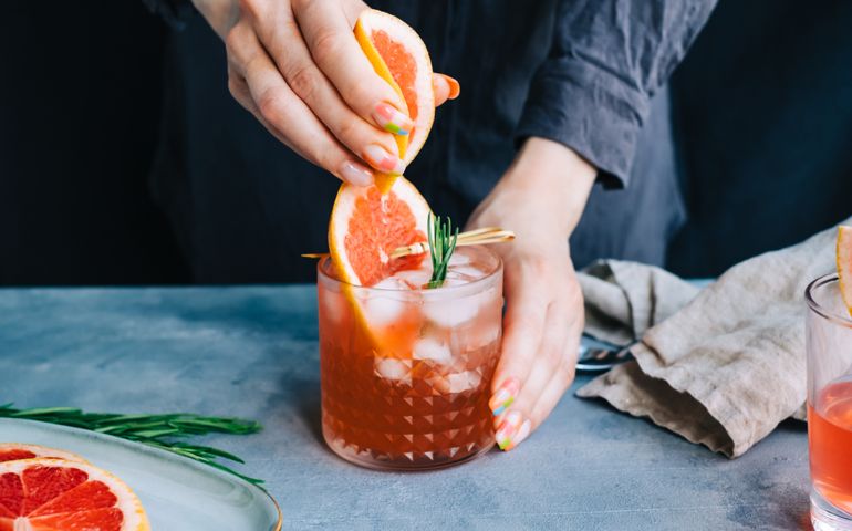 Female bartender hand squeezes juice from fresh grapefruitÂ in cocktail lemonade with ice and rosemary.