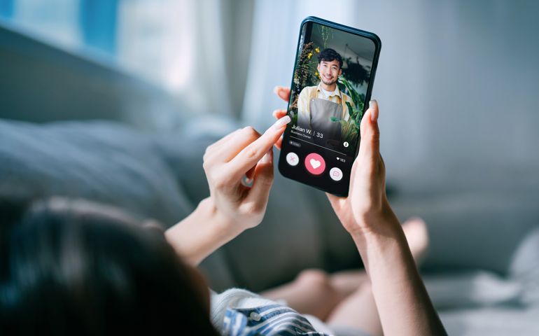 Young Asian woman lying on sofa at home, using an online dating app on smartphone, looking for love on the internet. Social media. Internet dating. Couple relationship. Love concept