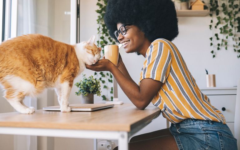 Happy woman with coffee cup looking at cat on desk