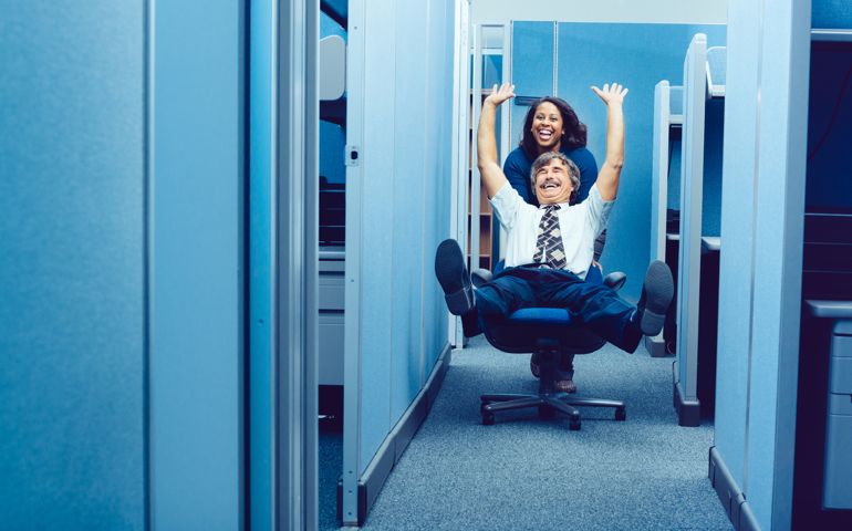 Co-workers racing through cubicles with office chair.