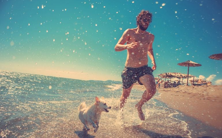 full body shot of young man running with his dog on the beach