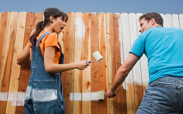 Multi-ethnic couple painting fence