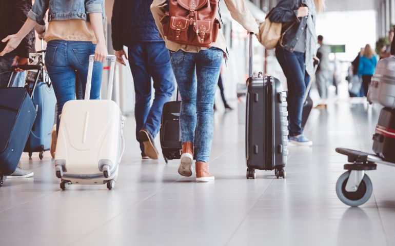 Low angle rear view of passengers walking in the airport terminal. People with luggage in airport.