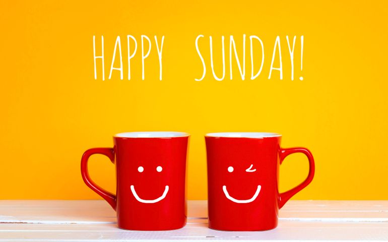 Two red coffee mugs with a smiling faces on a yellow background with the phrase Happy sunday. Happy coffee mugs.