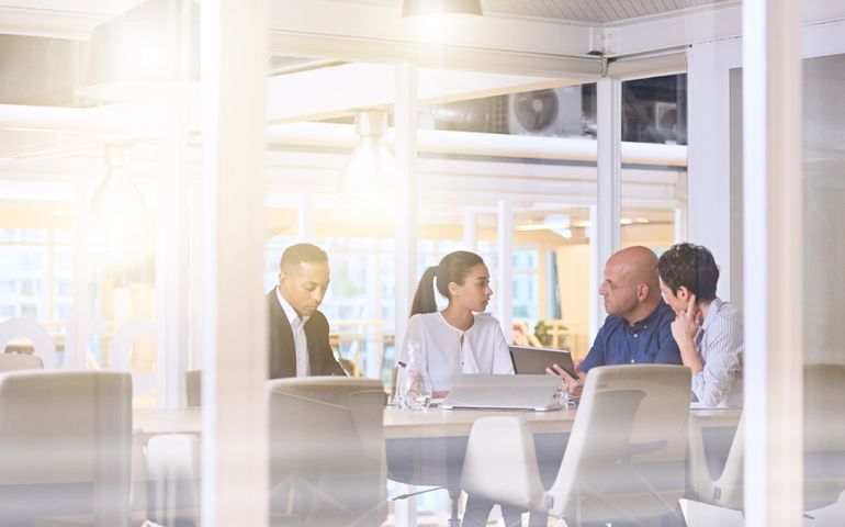 Corporate business meeting in modern office with glass walls, flare from the sunlight and reflections on the glass while business discussions take place amongst board members.