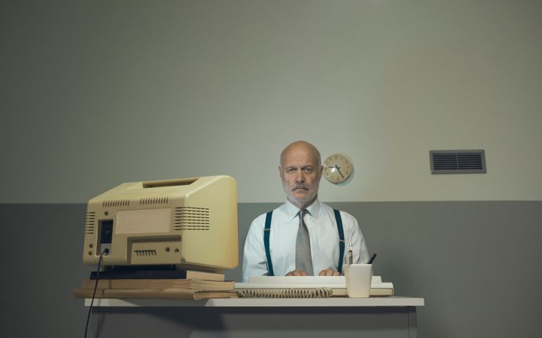 Sad senior businessman working with an outdated computer on a small desk, he is sad and disappointed