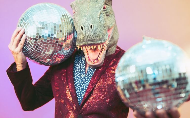 Senior man having fun wearing t-rex mask in discotheque - Elegant dinosaur masquerade male celebrating carnival party inside disco club - Funny absurd holidays and crazy people humor lifestyle concept