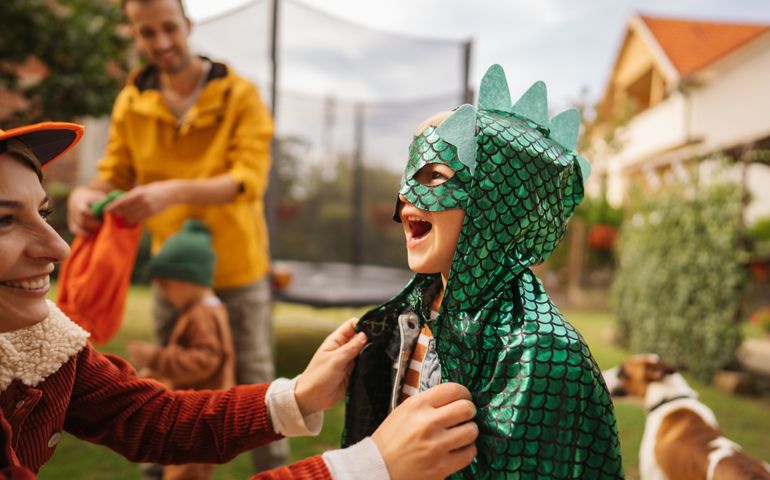 Photo of a little boy getting ready for the Halloween party with his mom in the backyard of their house.