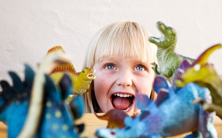 This pretty little blonde 3 year old roars back at her snarling toy dinosaurs, obviously not a bit scared! Focus is on the little girl.