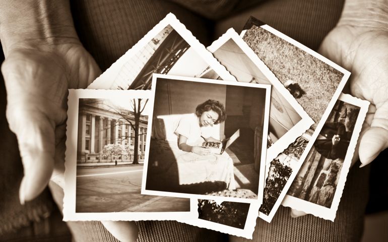 Toned image of an elderly, senior woman holding old vintage photographs of herself and of other places in her hands, showing her sentimental memories, past, and places travelled. Only her hands are shown in the image