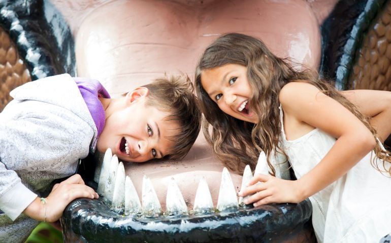 Two happy children are having fun pretending to be in the dinosaur jaw