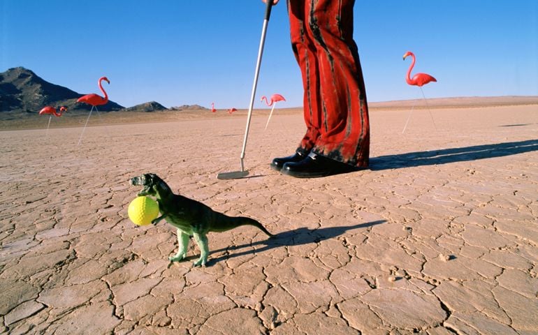 Toy dinosaur with golf ball in desert