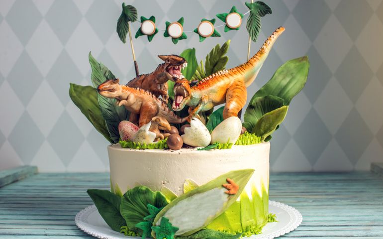 Children's holiday white cake decorated with mastic figurines of dinosaurs in the Jurassic period jungle. Concept ideas desserts for kids