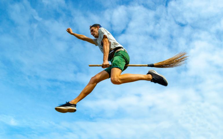 Young man flying on the broom with outstretched arm in the blue sky of Siquijor