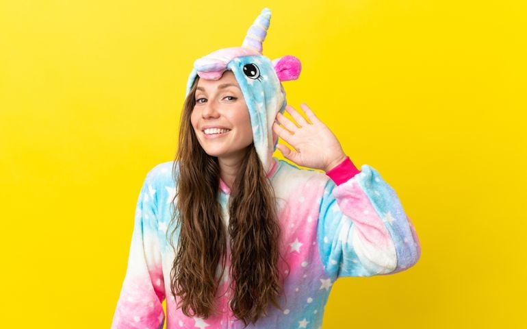 Girl with unicorn pajamas over isolated background listening to something by putting hand on the ear