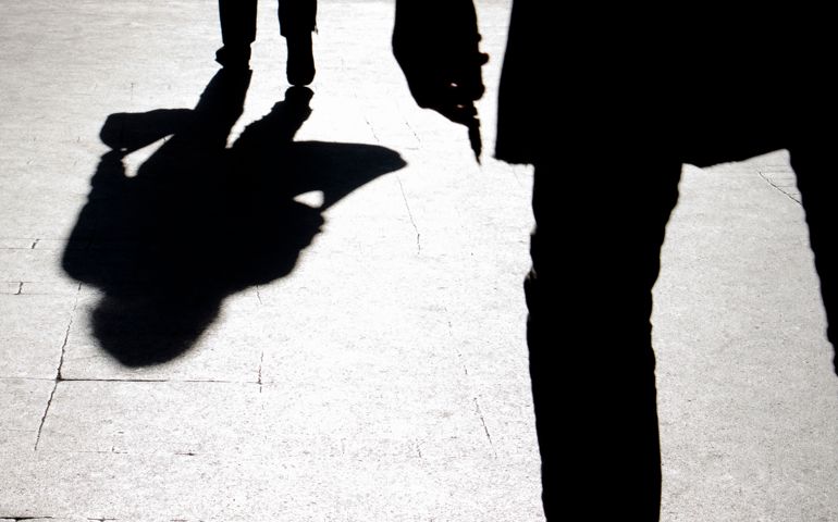 Blurry silhouette and shadow of a woman carrying a bag and a man holding sharp object following her, in the city street in the night