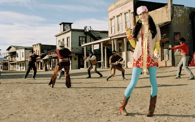 Girl posing with cowboys having gun duel in background