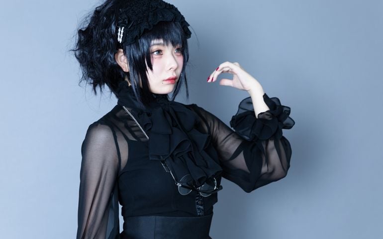 Portrait of Japanese young woman wearing black gothic dress. Looks like Harajuku, Tokyo style. Studio shot. Standing like a doll.
