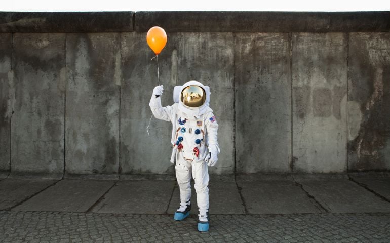 An astronaut on a city sidewalk holding a balloon
