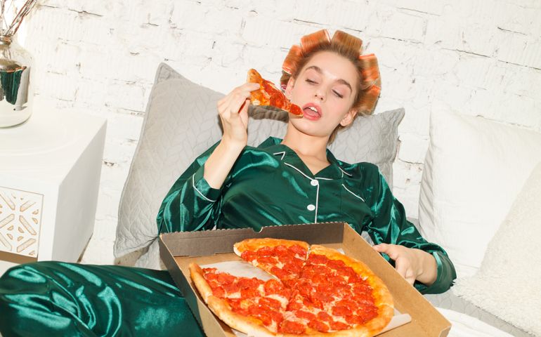 young sexy lazy woman in pajamas lying in bed and eating big pizza