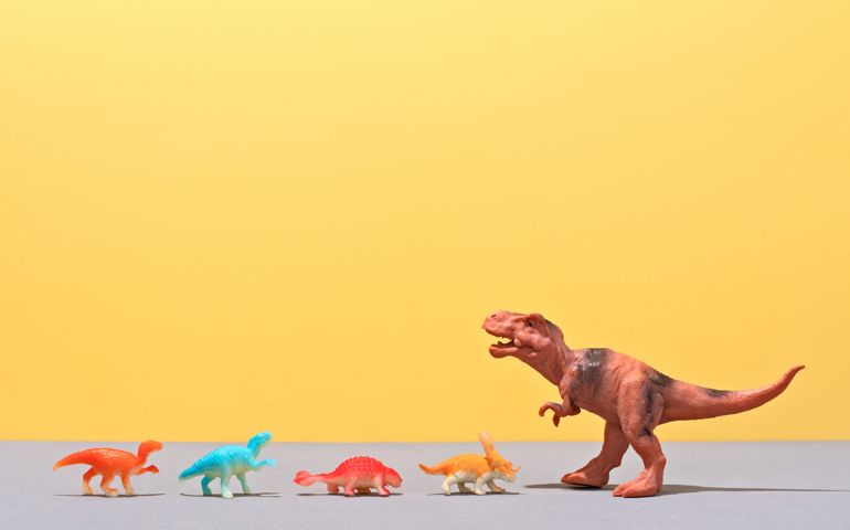Small Toy Dinosaurs Facing A Large Toy Dinosaur on Yellow Colored Background.
