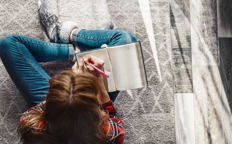 Young woman sitting on the floor at living room and writing into her diary