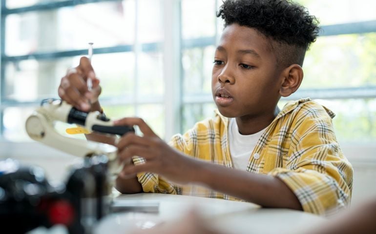 Genius School boy African American in technology class, while practice robot arm assembly and program coding.