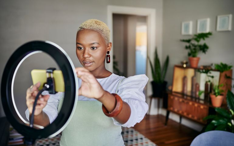 Young African female influencer adjusting a smart phone and ring light before doing an online vlog post at home