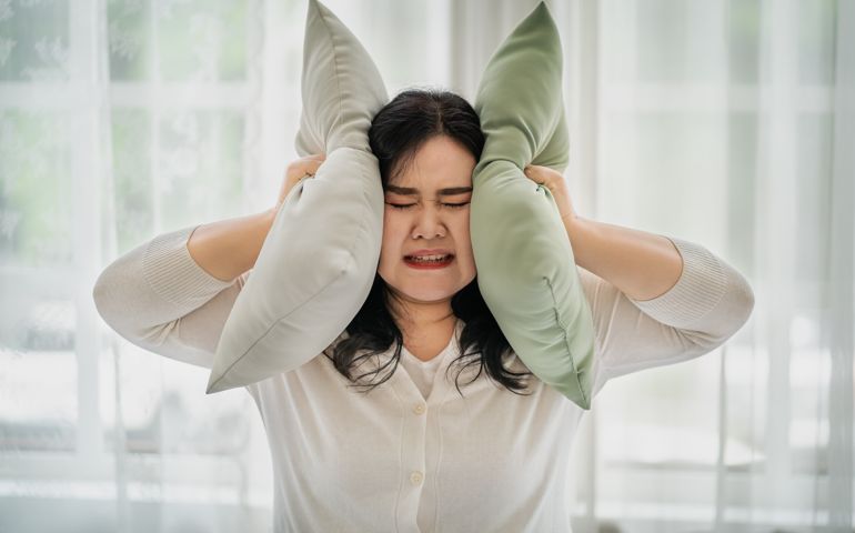 Fat woman covering her ears with a pillow, the concept does not want to hear things. affecting oneself