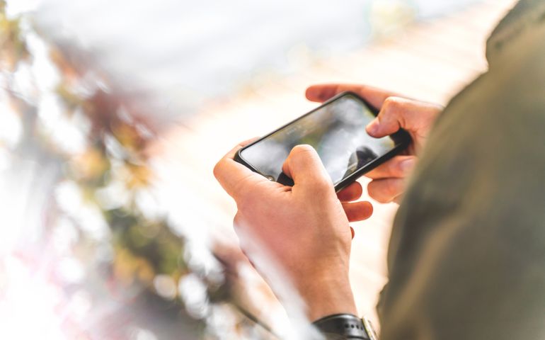 A man using a mobile phone illustrating the technological concepts and Internet communication in 2022 green and olive colors. Holding a smartphone with both hands in horizontal mode, playing games, or watching video