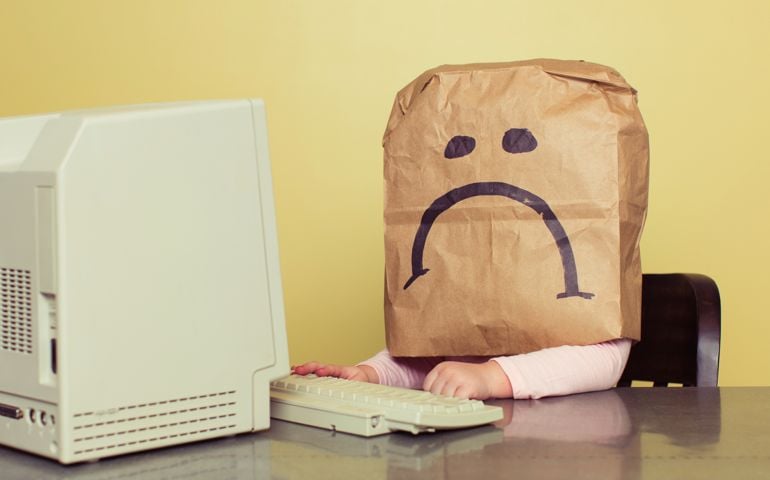 A young girl sits at a computer and has a big sad face. This young person has been a victim of cyber bullying. Stop bullying.