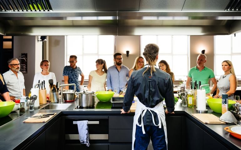 Young chef standing behind a modern kitchen and welcoming his cooking class