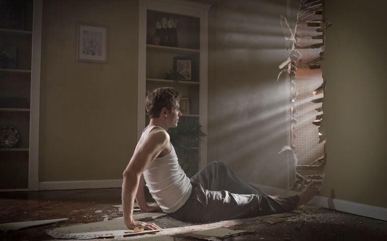 man on floor looking back through hole in wall