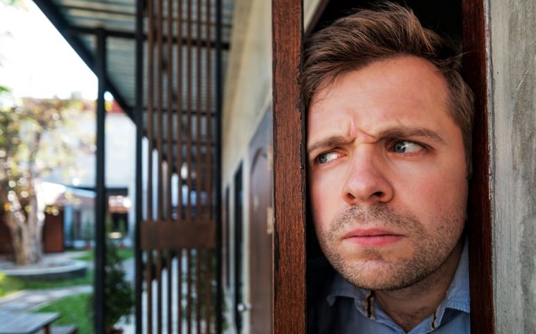 Young caucasian man with agoraphobia spying and looking out the door. He is afraid of communication with people