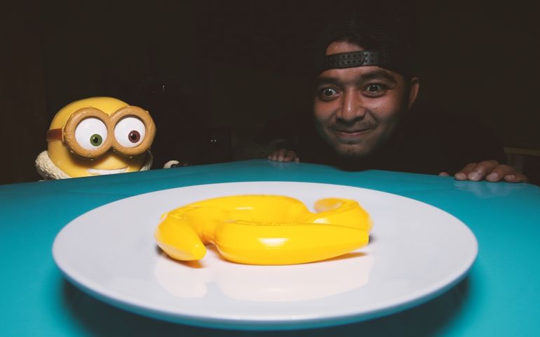 A man and a minions stare at bananas in a plate on the blue plastic table
