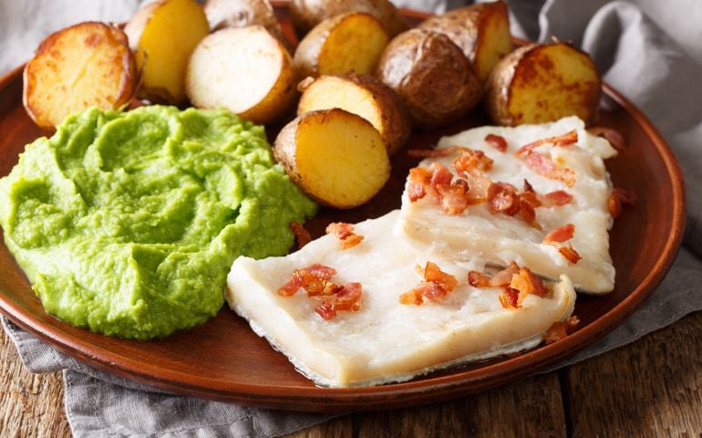 Cod Lutefisk with pea puree, baked potatoes and bacon close-up on a plate on the table. horizontal